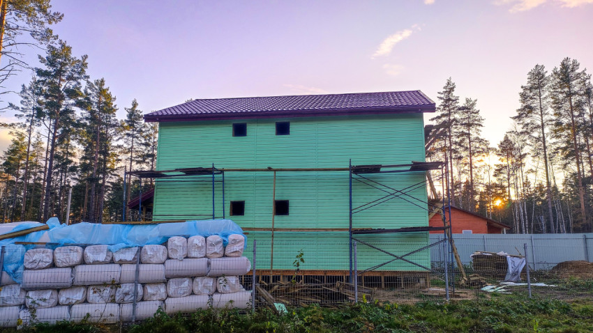 Двухэтажный дом с зелёным фасадом и строительными материалами на участке