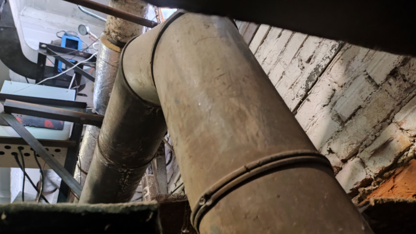 Участок металлического трубопровода рядом с кирпичной стеной