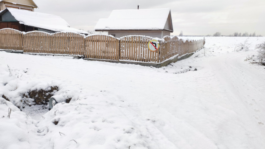 Сельская улица в зимний период с жилыми постройками и ограждением