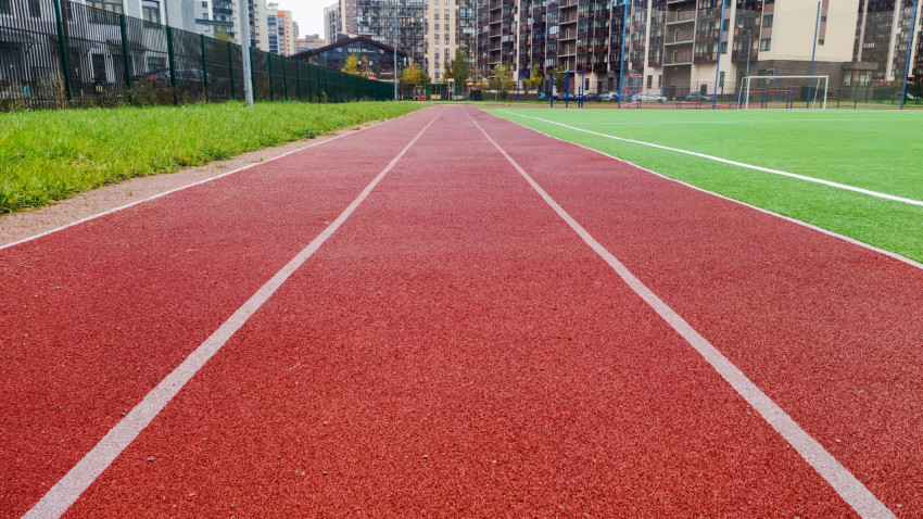 Красная беговая дорожка рядом с футбольным полем и жилыми домами