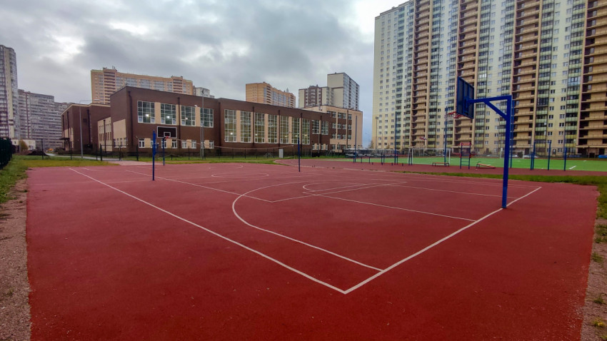 Баскетбольная площадка у школьного здания с футбольным полем на заднем плане