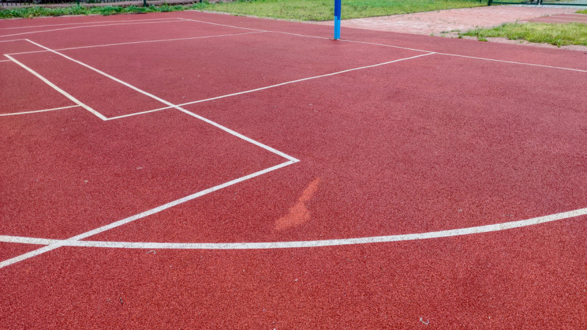 Поверхность спортивной площадки с дефектом покрытия и линиями разметки