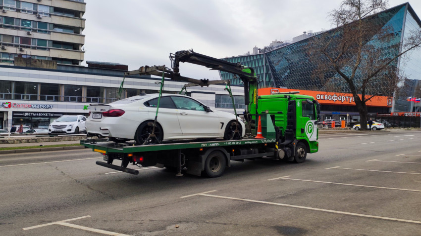 Эвакуатор перевозит легковой автомобиль на городской улице