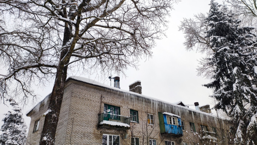 Советский кирпичный жилой дом зимой с крупными сосульками на крыше