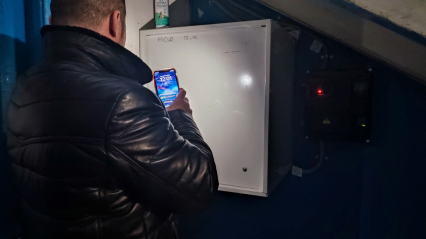 Мужчина освещает фонариком электрический шкаф в подъезде