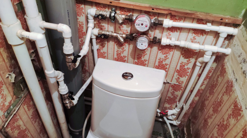 Сантехнические трубы и водомеры за унитазом в санузле