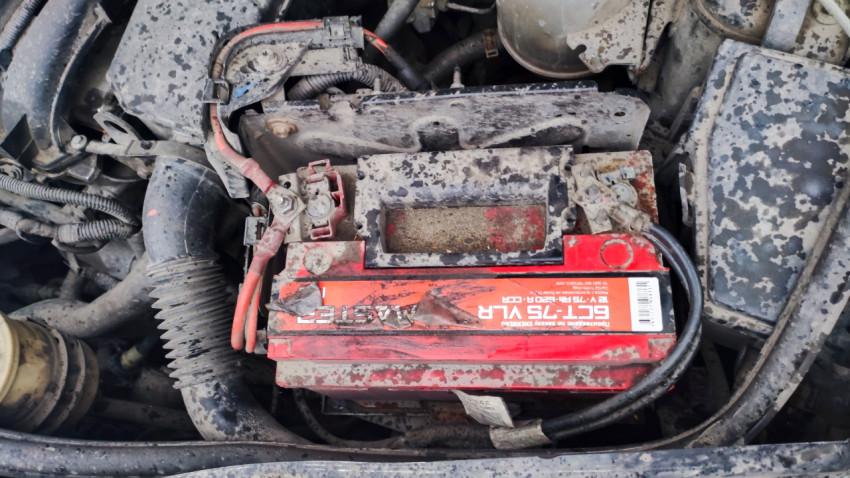 Автомобильный аккумулятор под капотом в грязном отсеке двигателя