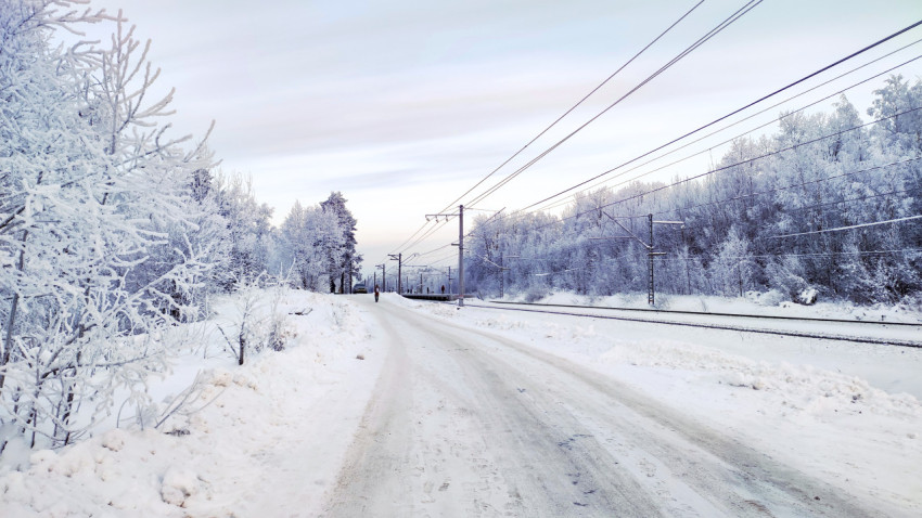 Заснеженная дорога вдоль железнодорожных путей зимой
