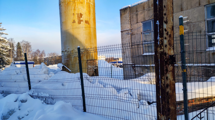 Основание трубы и производственный корпус за ограждением
