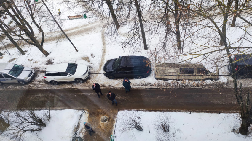 Улица под балконом с припаркованными автомобилями и прохожими