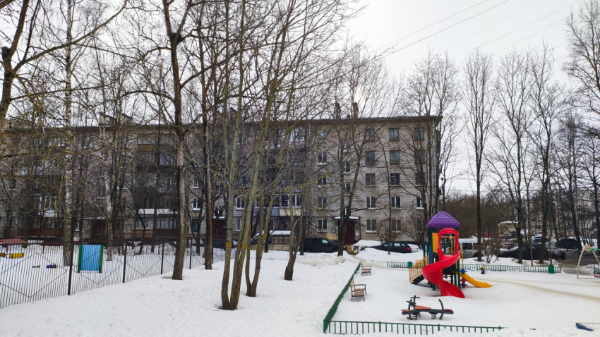 Жилая пятиэтажка и детская площадка во дворе зимой