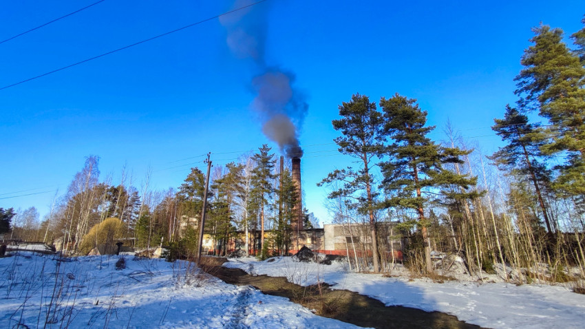 Промышленная труба с черным дымом над зимним пейзажем