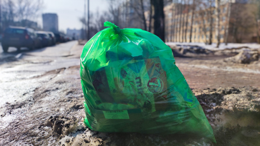 Зеленый мусорный пакет на обочине в период снеготаяния