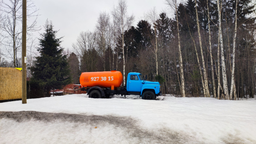 Синий грузовик с оранжевой цистерной на заснеженной площадке