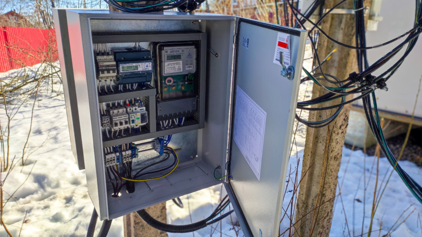 Электрощит с открытой дверцей на опоре в загородном посёлке