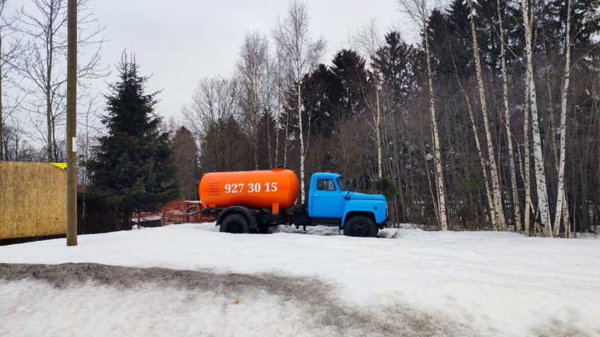 Синий грузовик с оранжевой цистерной на фоне зимнего леса