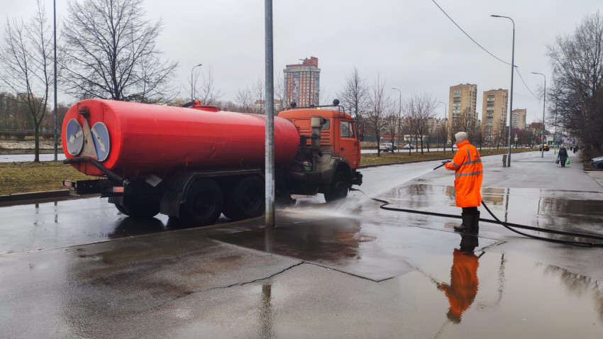 Рабочий с водовозом моет тротуар на улице города