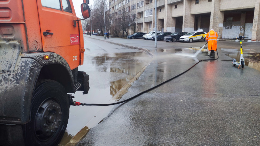 Рабочий коммунальных служб моет асфальт возле жилого дома