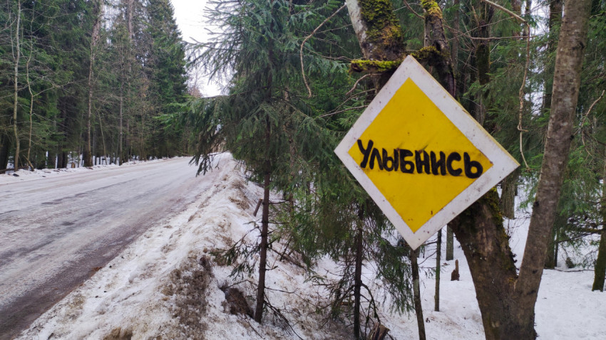 Дорога и знак «Улыбнись» у обочины зимнего леса