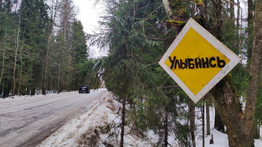 Лесная дорога зимой и знак с надписью «Улыбнись»