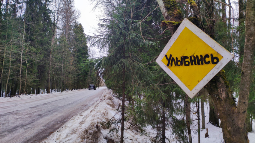 Самодельный знак «Улыбнись» у зимней дороги в лесу