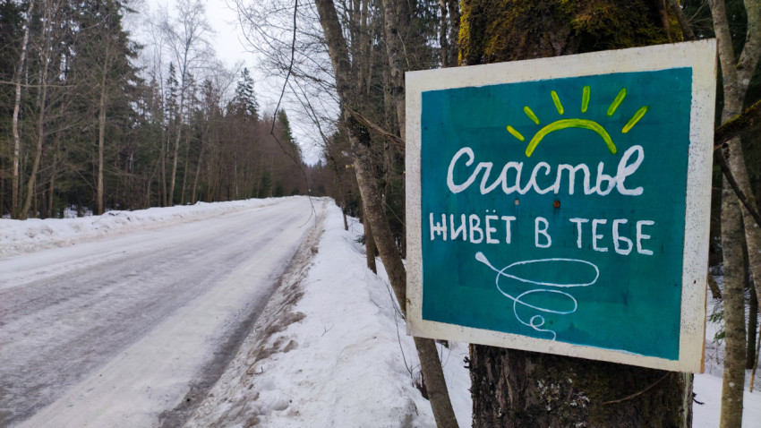 Уличный знак «Счастье живёт в тебе» на фоне зимней дороги