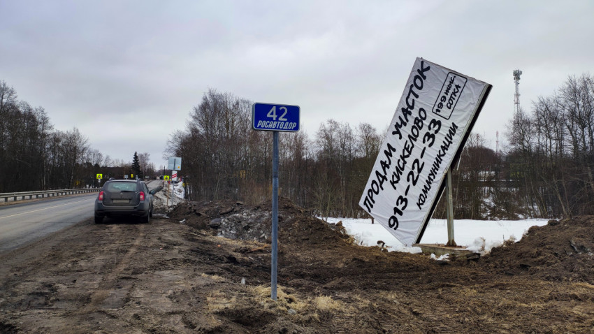 Повреждённый рекламный щит и автомобиль у обочины зимой