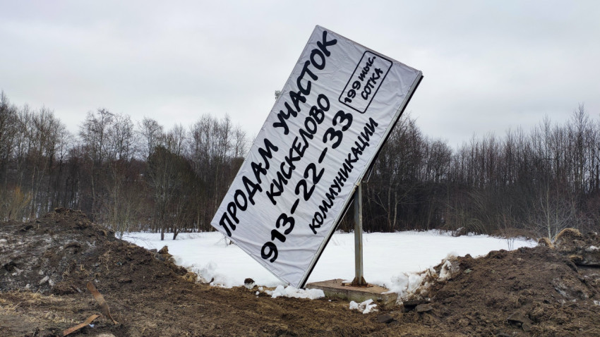 Наклонённый рекламный щит о продаже участка в деревне Кискелово