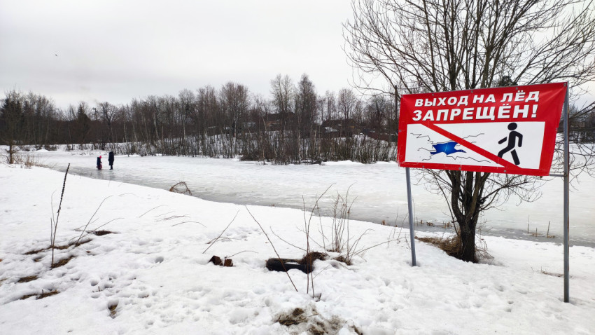 Знак «Выход на лёд запрещён» у замерзшего пруда с людьми на льду