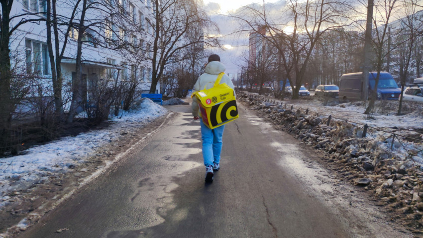 Курьер Яндекс Еда идет по тротуару в зимнем городе