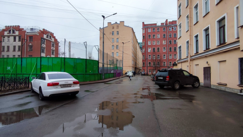 Двор между жилыми домами с парковкой и зелёным ограждением