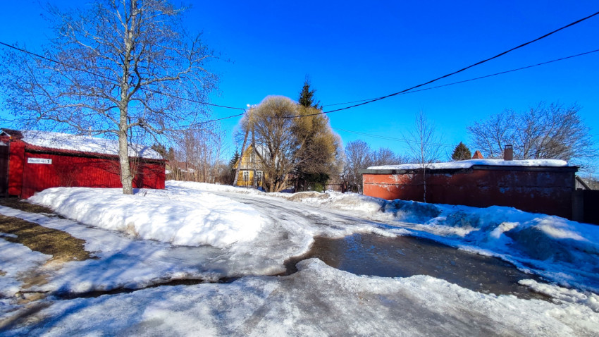 Загородная улица с тающим снегом и частной застройкой
