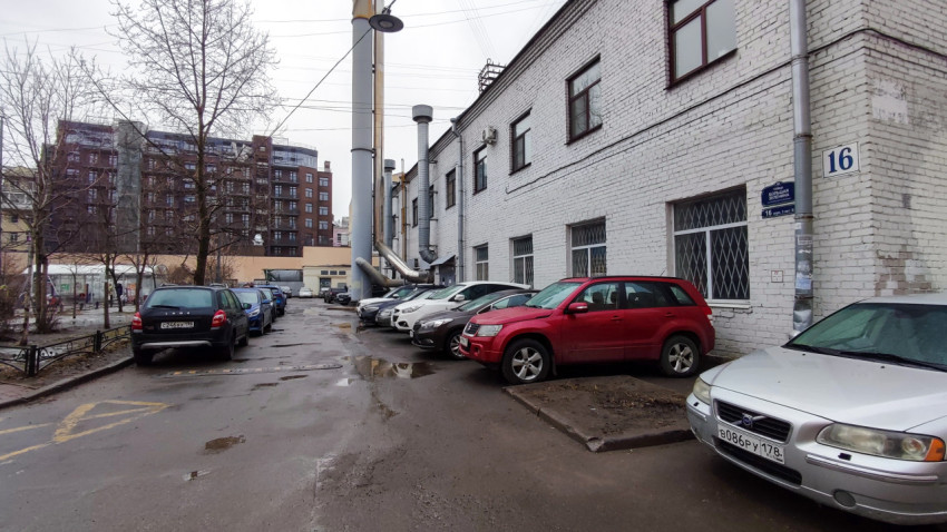 Парковка у белого кирпичного здания на улице с деревьями