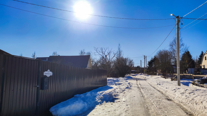 Улица с забором и опорами электросети под зимним солнечным светом
