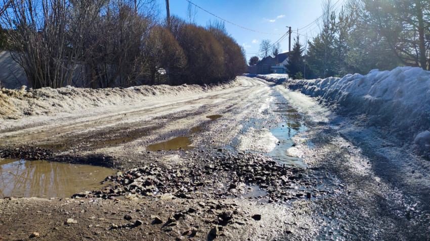 Размытая грунтовая дорога с лужами и снегом по обочинам