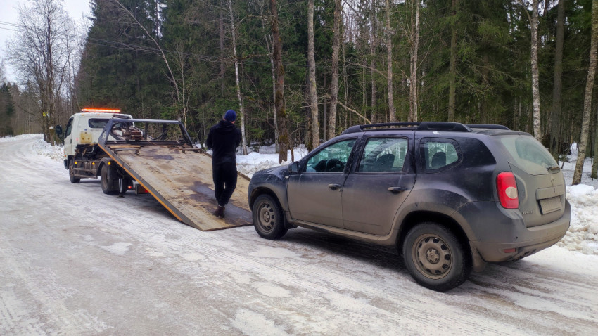 Рабочий закрепляет автомобиль Renault Duster на эвакуаторе в зимнем лесу