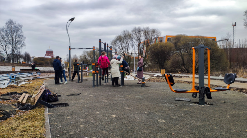 Спортивная площадка с тренажёрами и жителями на фоне благоустраиваемого парка