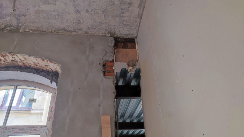 Участок стены с повреждённой штукатуркой и металлическим перекрытием