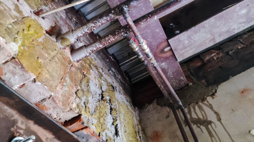 Металлические трубы и балки перекрытия на фоне старой кирпичной стены