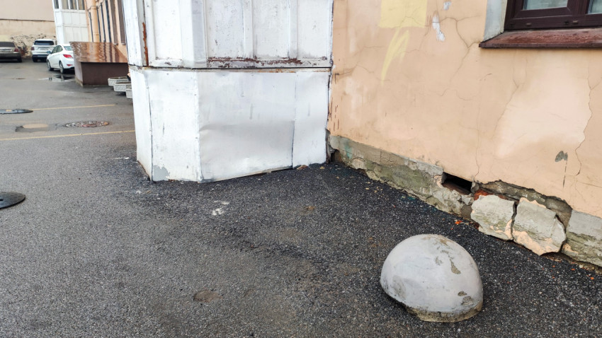 Старая стена с трещинами и бетонным ограничителем во дворе жилого дома