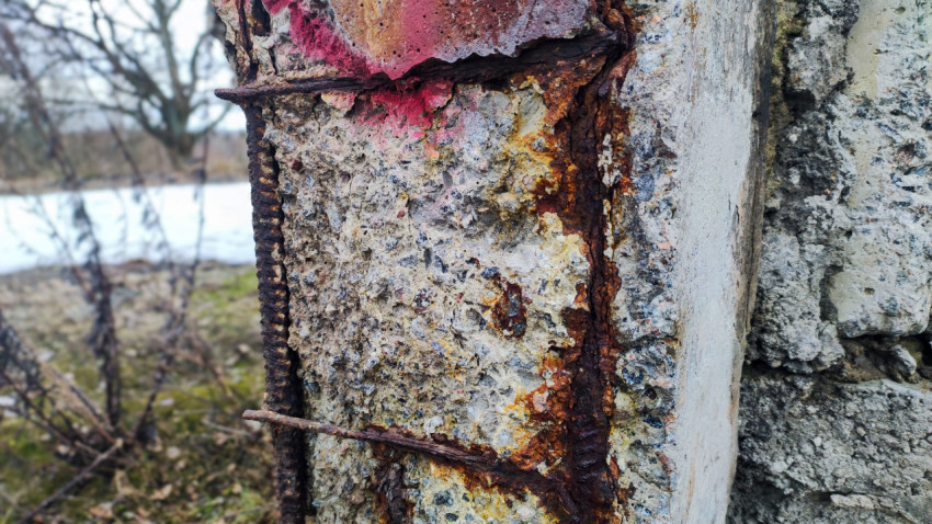 Ржавеющая арматура в разрушенном бетонном столбе на фоне зимнего пейзажа