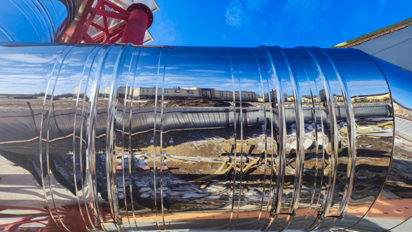 Полированная поверхность дымовой трубы с отражением зданий