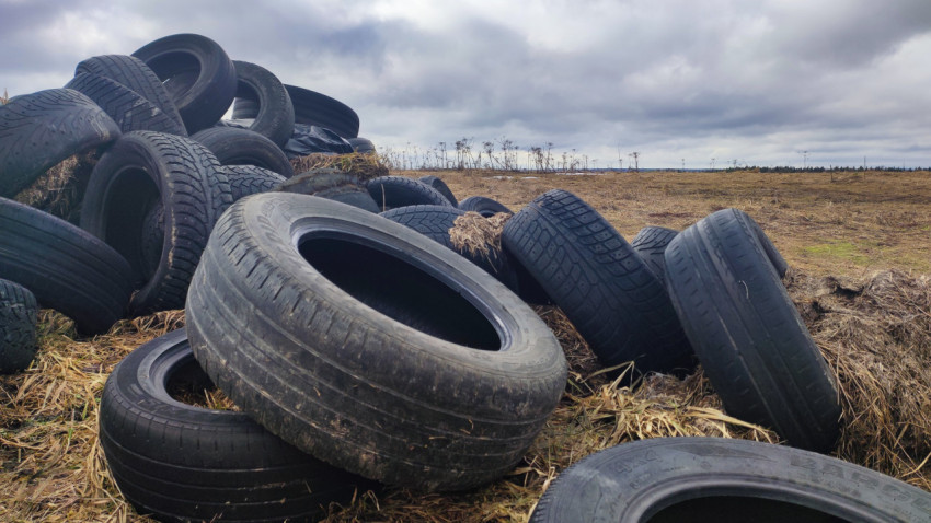 Автомобильные шины, сложенные на поле, под облачным небом