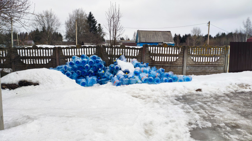 Скопление пластиковых бутылей для воды у бетонного забора