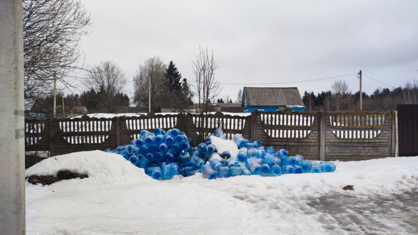 Пластиковые бутыли для воды, сложенные у частного забора