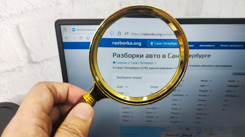 Лупа в руке перед экраном ноутбука с сайтом авторазборки