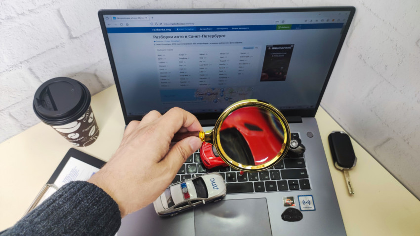 Лупа над ноутбуком с модельными автомобилями и сайтом авторазборки