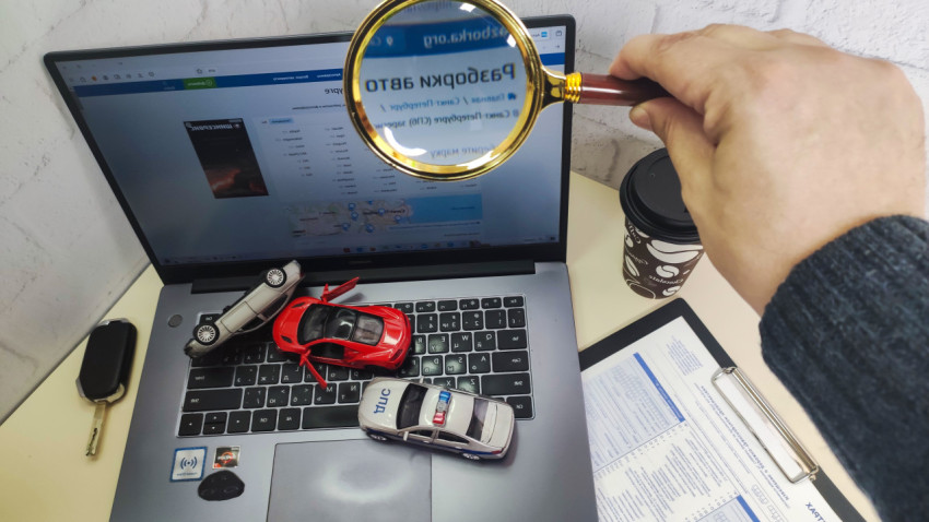 Лупа над ноутбуком с моделями машин и документами ОСАГО