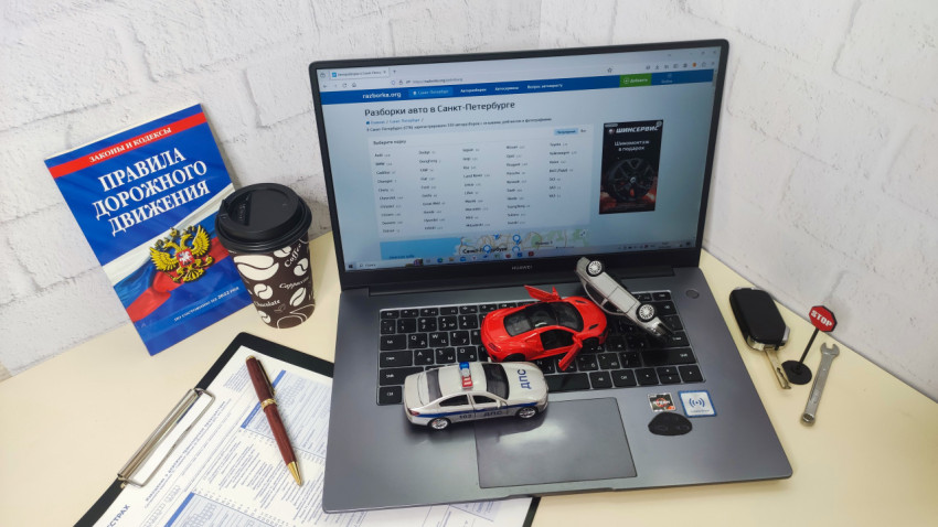 Стол с ноутбуком и справочником ПДД рядом с модельными автомобилями