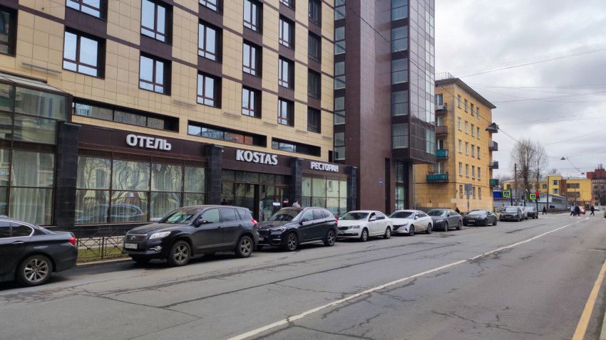 Фасад отеля Kostas и линия припаркованных автомобилей на городской улице